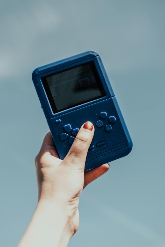 A close-up of a hand holding a vintage blue gaming console against a clear sky.