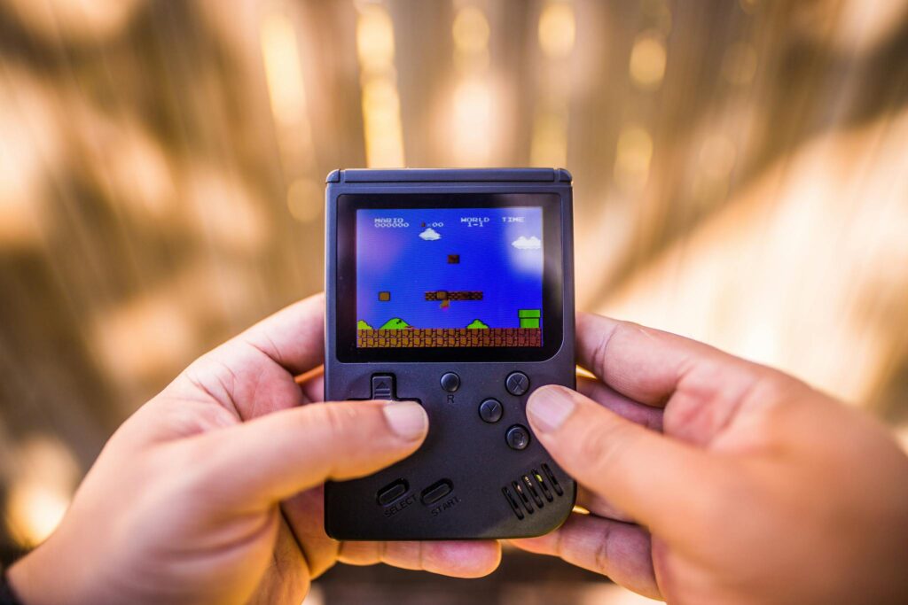 A close-up of hands holding a retro game console playing a classic Mario game outdoors.