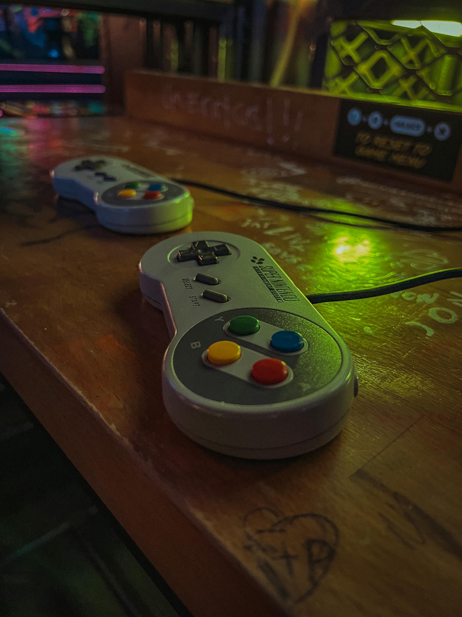 Close-up of two retro gaming controllers on a wooden table with ambient colorful lighting.