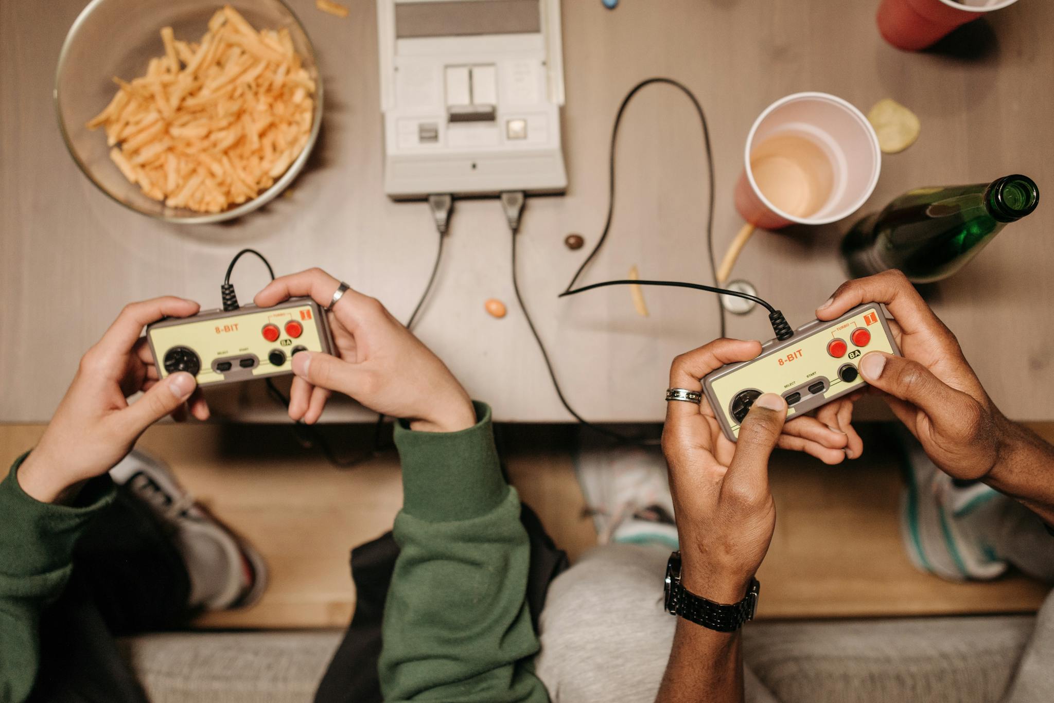 Two friends enjoying a classic gaming session with 8-bit console controllers and snacks.